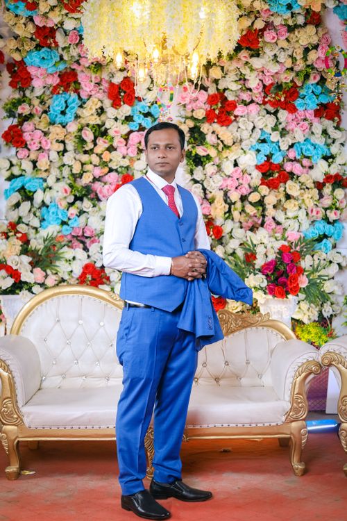 Free Elegant groom posing indoors with floral backdrop at Indian wedding. Stock Photo