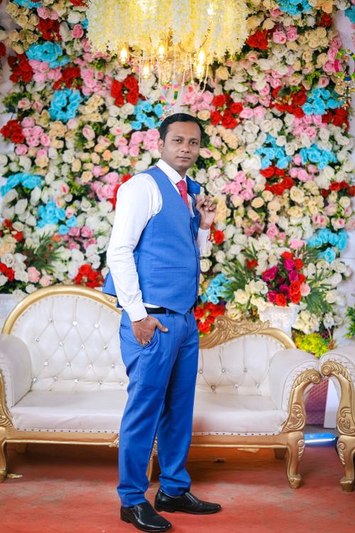 Free A man in formal attire poses confidently at an Indian wedding in front of a vibrant floral backdrop. Stock Photo