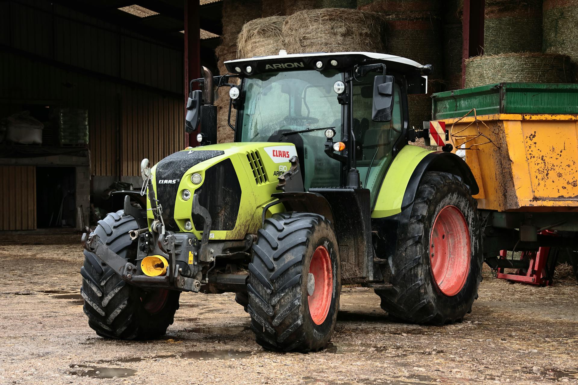 A green tractor with a trailer parked in front of a barn