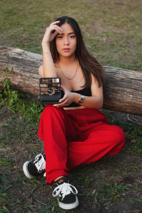 Free Stylish young woman in red pants posing with a vintage camera outdoors. Stock Photo
