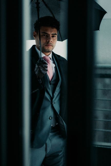 A stylish man in a suit holding an umbrella, captured indoors with a moody atmosphere.
