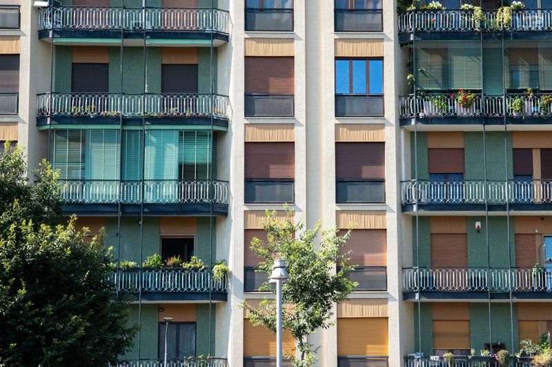 Contemporary apartment facade with glass balconies and green accents, capturing urban residential life.