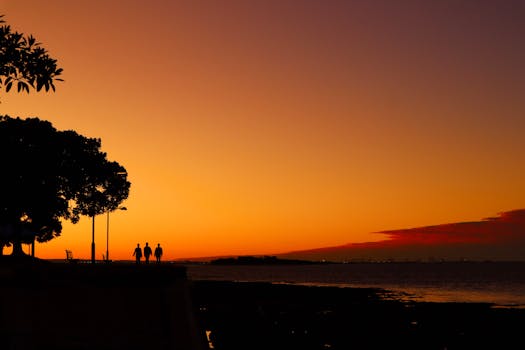 A serene sunset with silhouetted people by the sea, capturing warm tones and tranquility.
