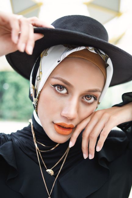 Stylish portrait of a woman in a hat and patterned hijab, enhancing elegance and fashion.