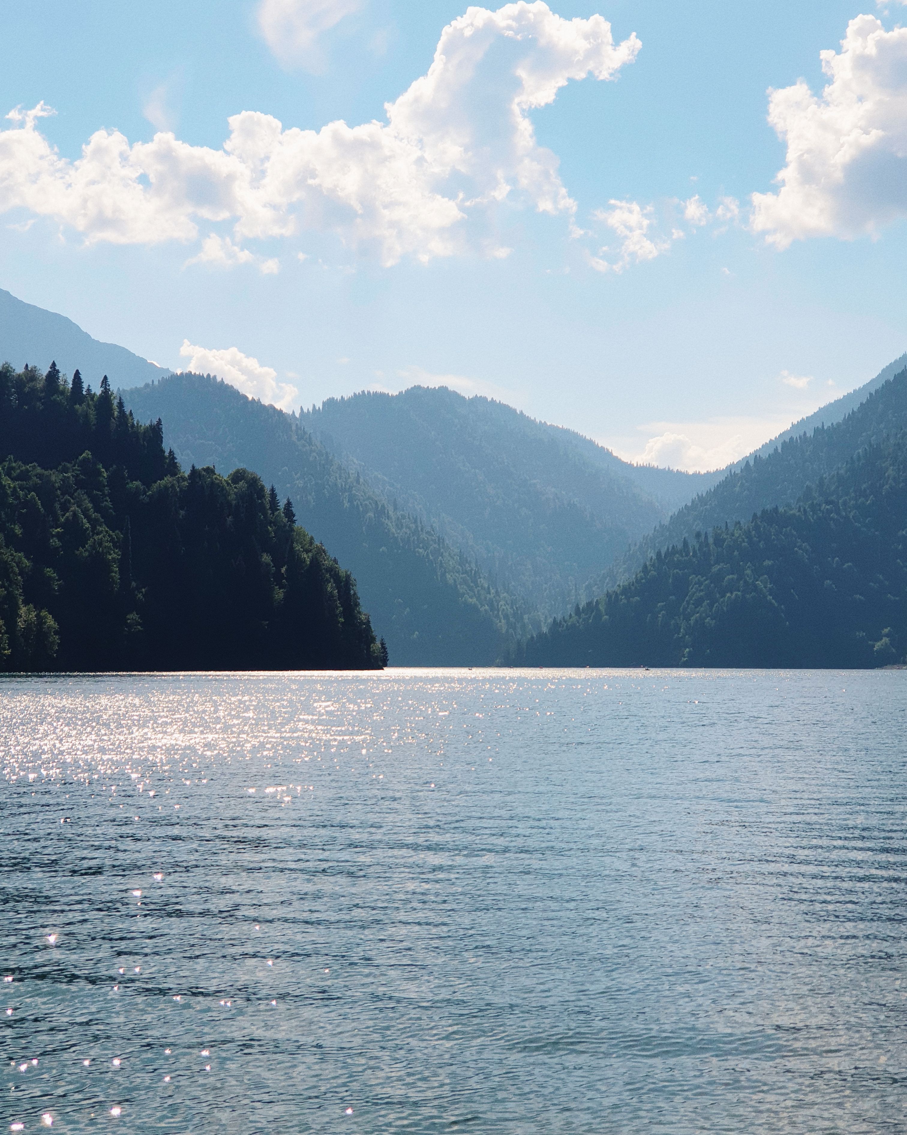 Serene view of a mountain lake with forested shores under a bright sky.