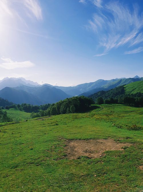 Free Breathtaking view of lush green hills with majestic mountains in the background on a sunny day. Stock Photo