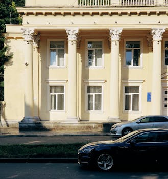 A majestic neoclassical building with columns, captured during the day with parked cars in front.
