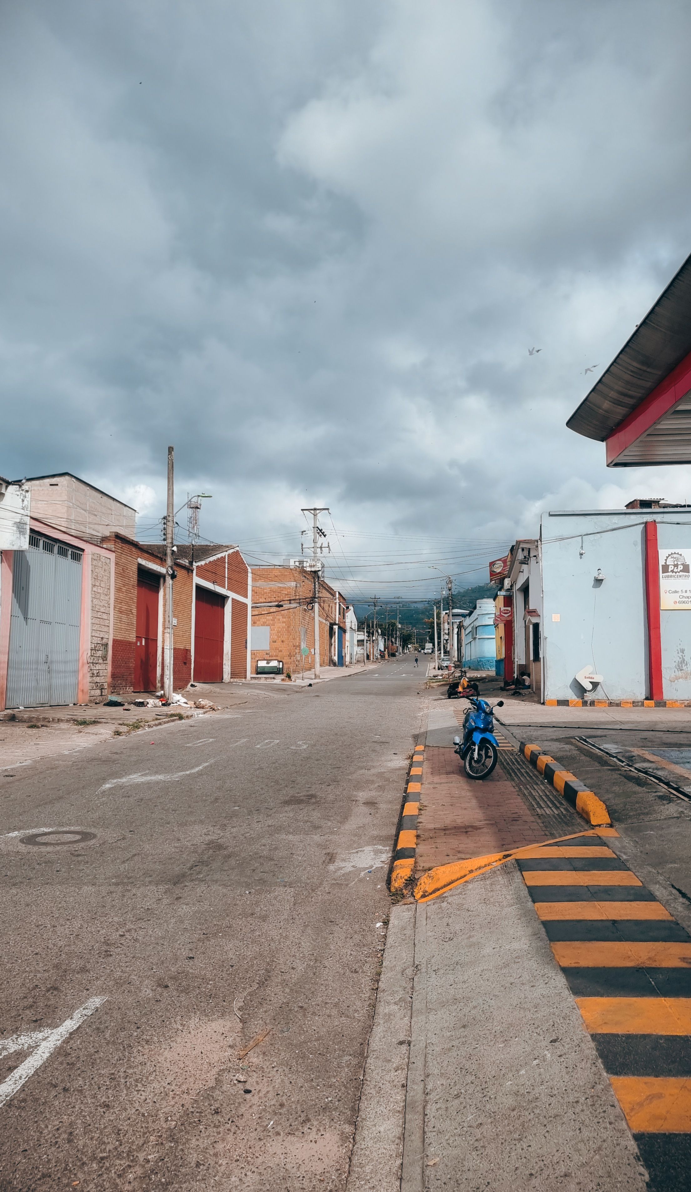 Desolate street in Bucaramanga, Colombia, under cloudy skies, featuring industrial buildings and a lone motorcycle.