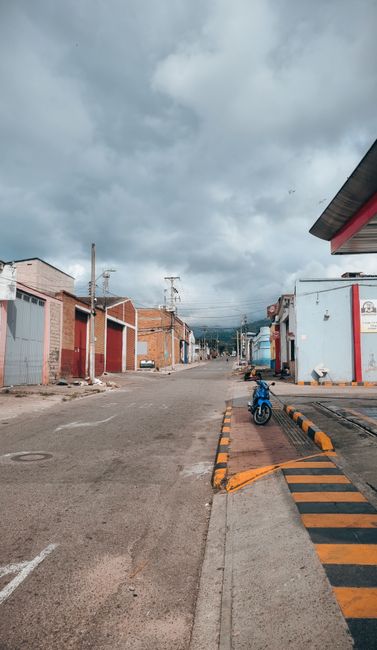 Fotomural Calle desolada en Bucaramanga, Colombia, bajo cielos nublados, con edificios industriales y una motocicleta solitaria.