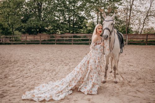 Free A woman in a floral dress stands gracefully with a white horse in an outdoor setting. Stock Photo