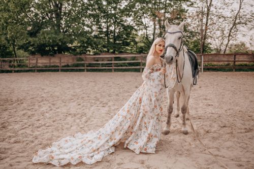 Free A woman in a floral dress standing next to a white horse outdoors on a sunny day. Stock Photo