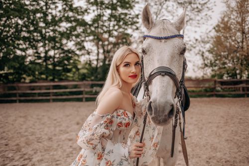 Free Elegant woman in floral dress posing with a white horse in a sunny outdoor setting. Stock Photo
