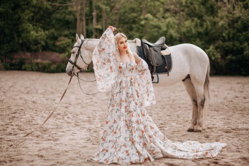Free A stylish woman poses with a horse, wearing a beautiful floral dress, in an outdoor setting. Stock Photo