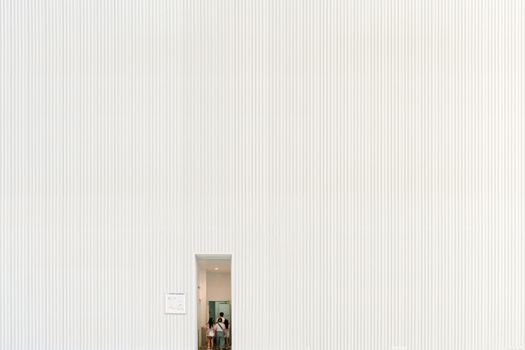 A large white textured wall with a small doorway entrance and visible people inside.