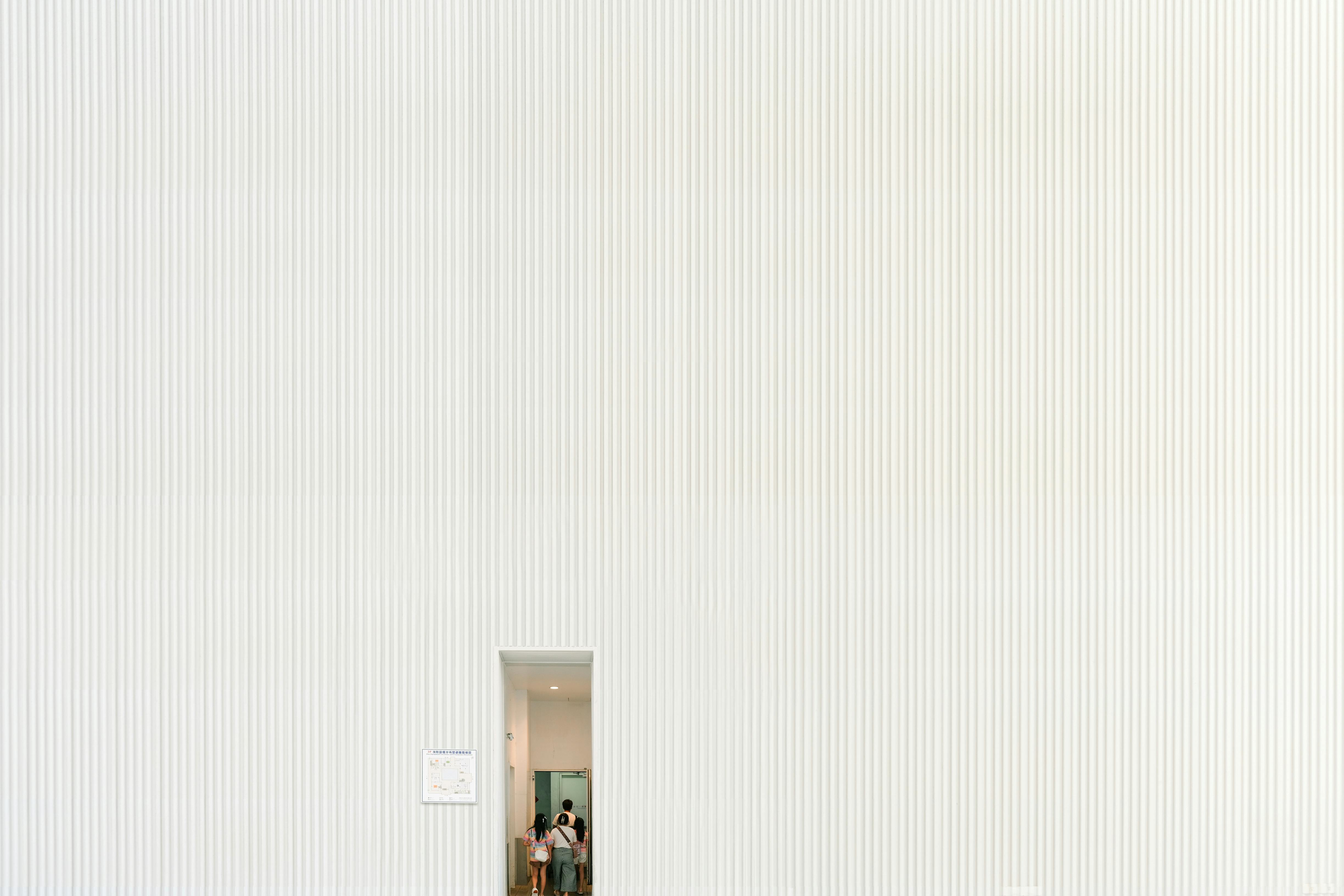 Free A large white textured wall with a small doorway entrance and visible people inside. Stock Photo