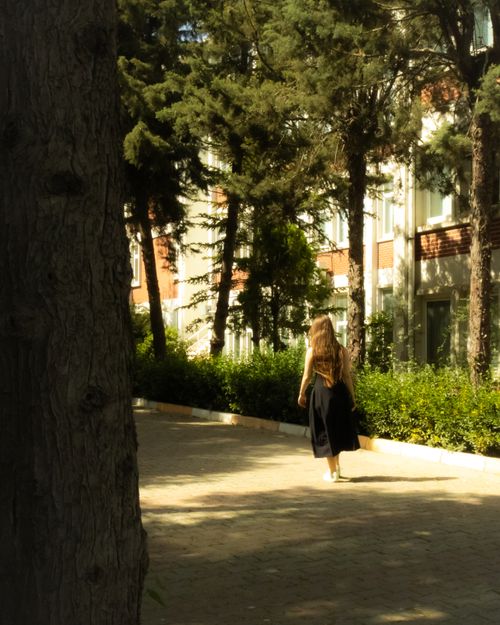 Free A woman in a dress walks in a sunlit park in Istanbul, surrounded by trees. Stock Photo
