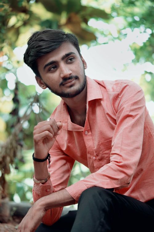 Free Portrait of a young man outdoors, posing casually in a stylish pink shirt with a thoughtful expression. Stock Photo