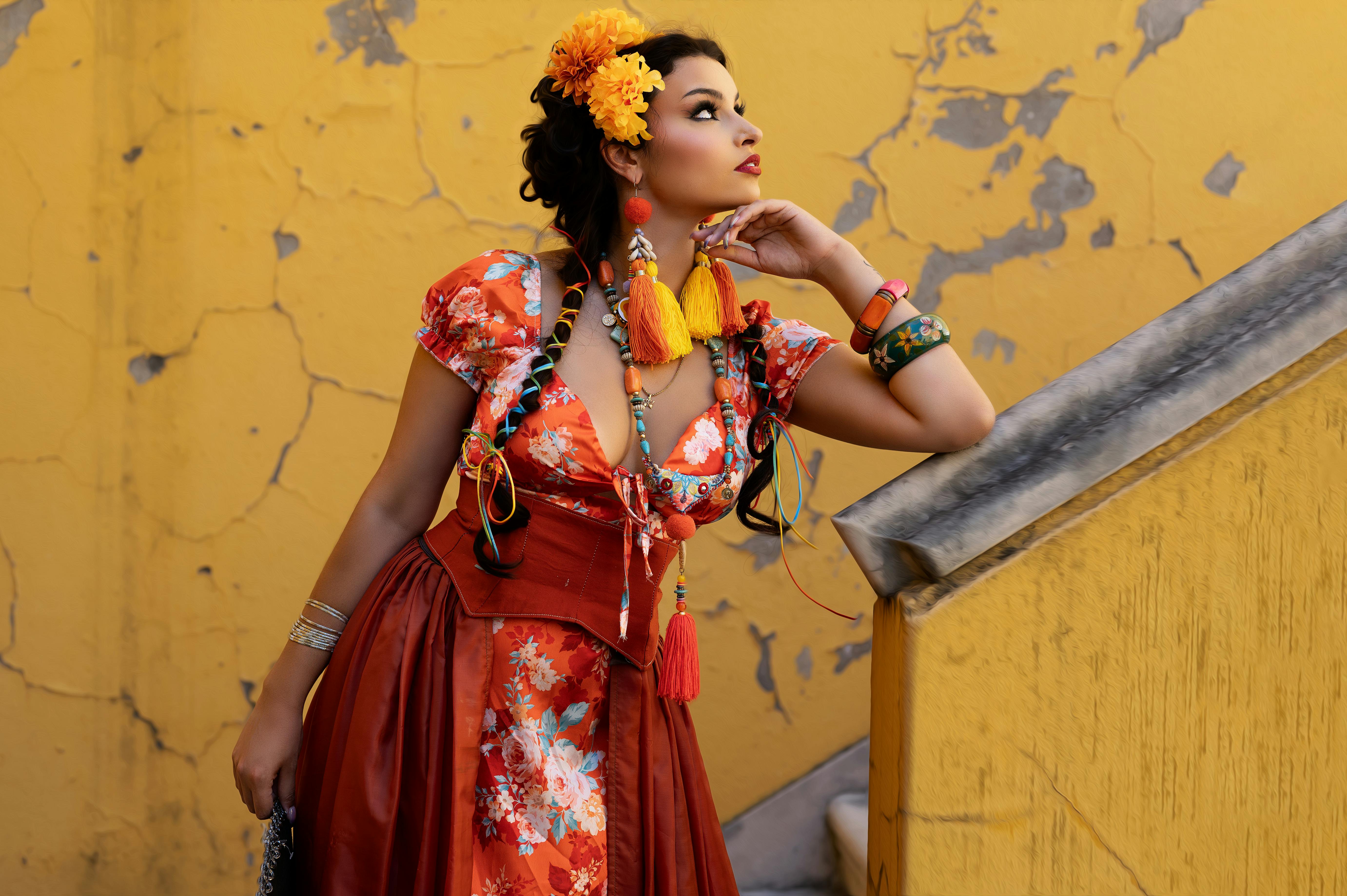 Fashionable woman in floral dress leans on stairs against a vibrant yellow wall.