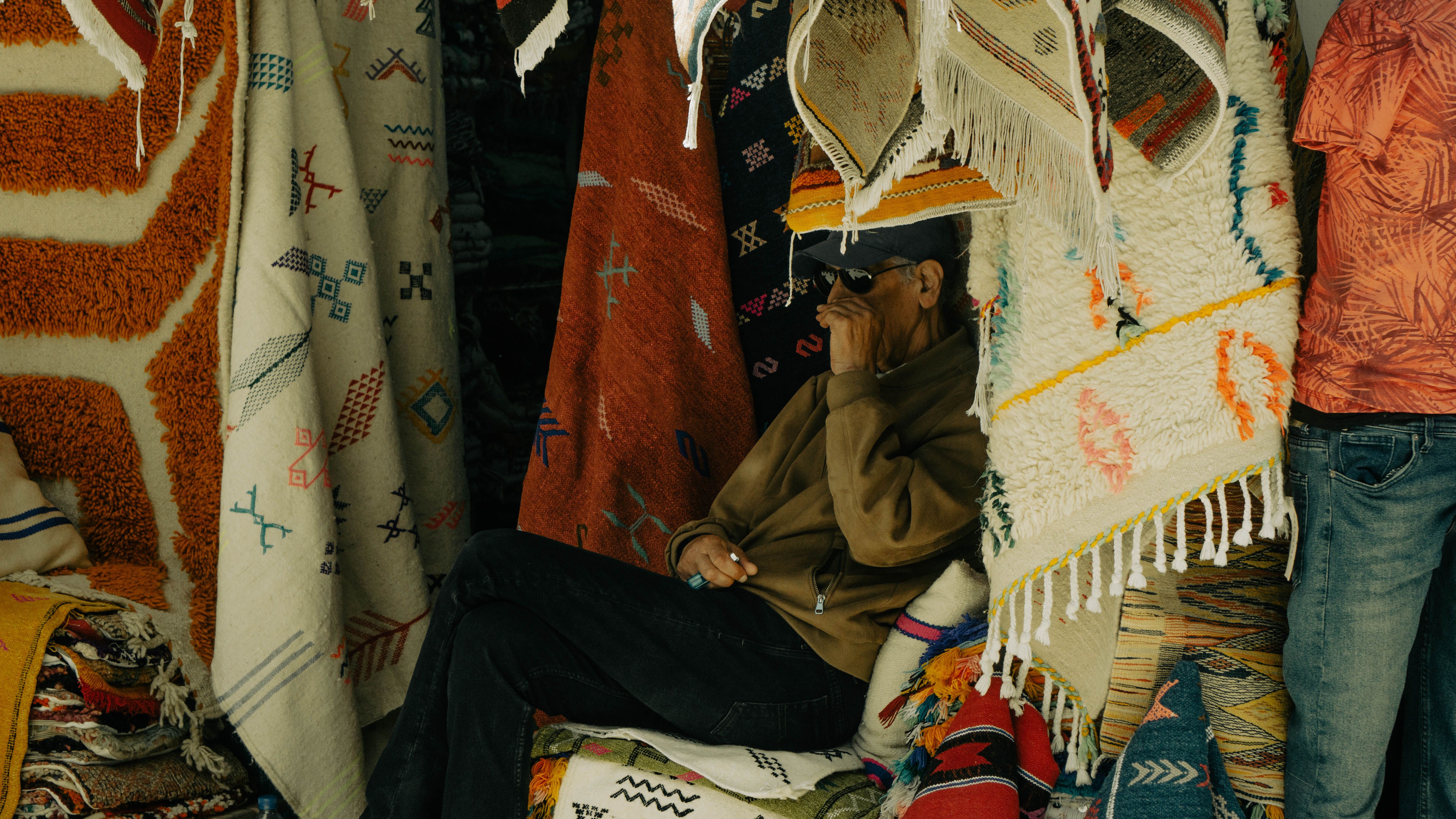 Man sitting among vibrant rugs in a market stall in Essaouira, Morocco.