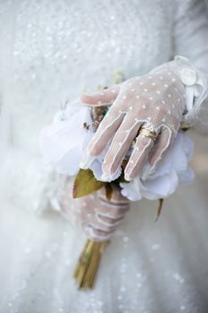 Close-up of a bride's lace-gloved hand holding a wedding bouquet.