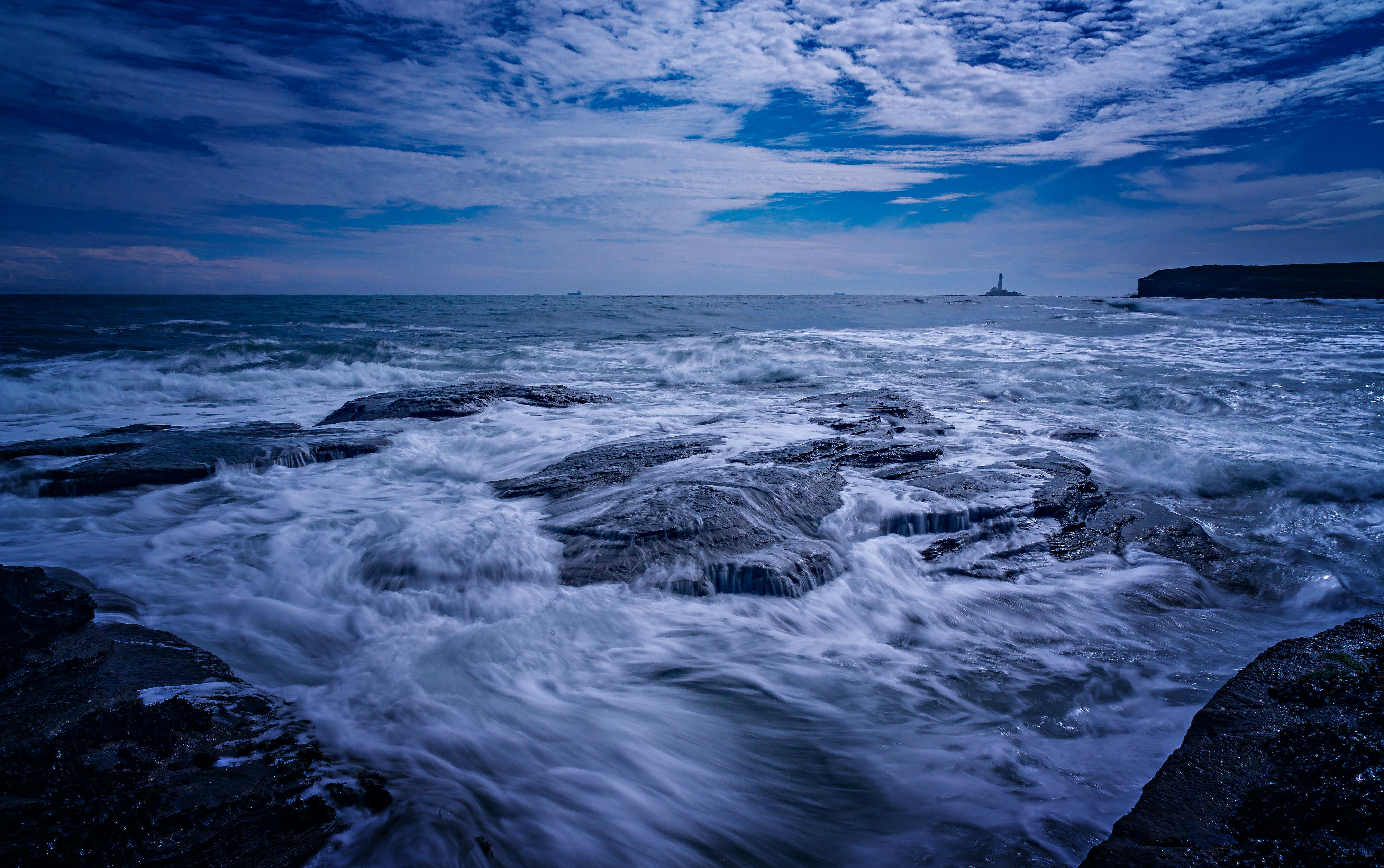 a blue sky with clouds and waves crashing on the rocks