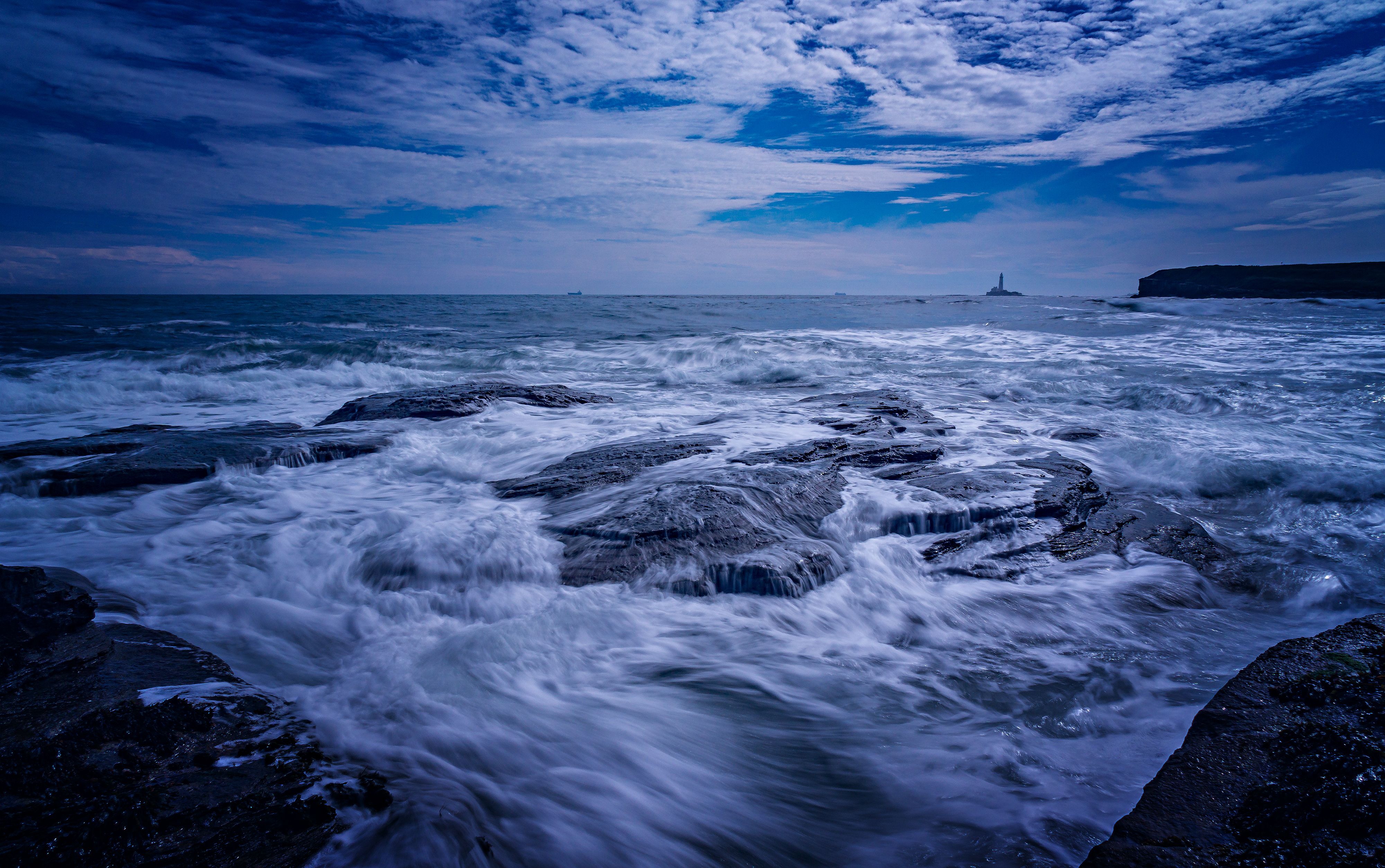 A blue sky with clouds and waves crashing on the rocks · Free Stock Photo
