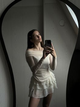 Stylish portrait of a woman in a white dress taking a mirror selfie.