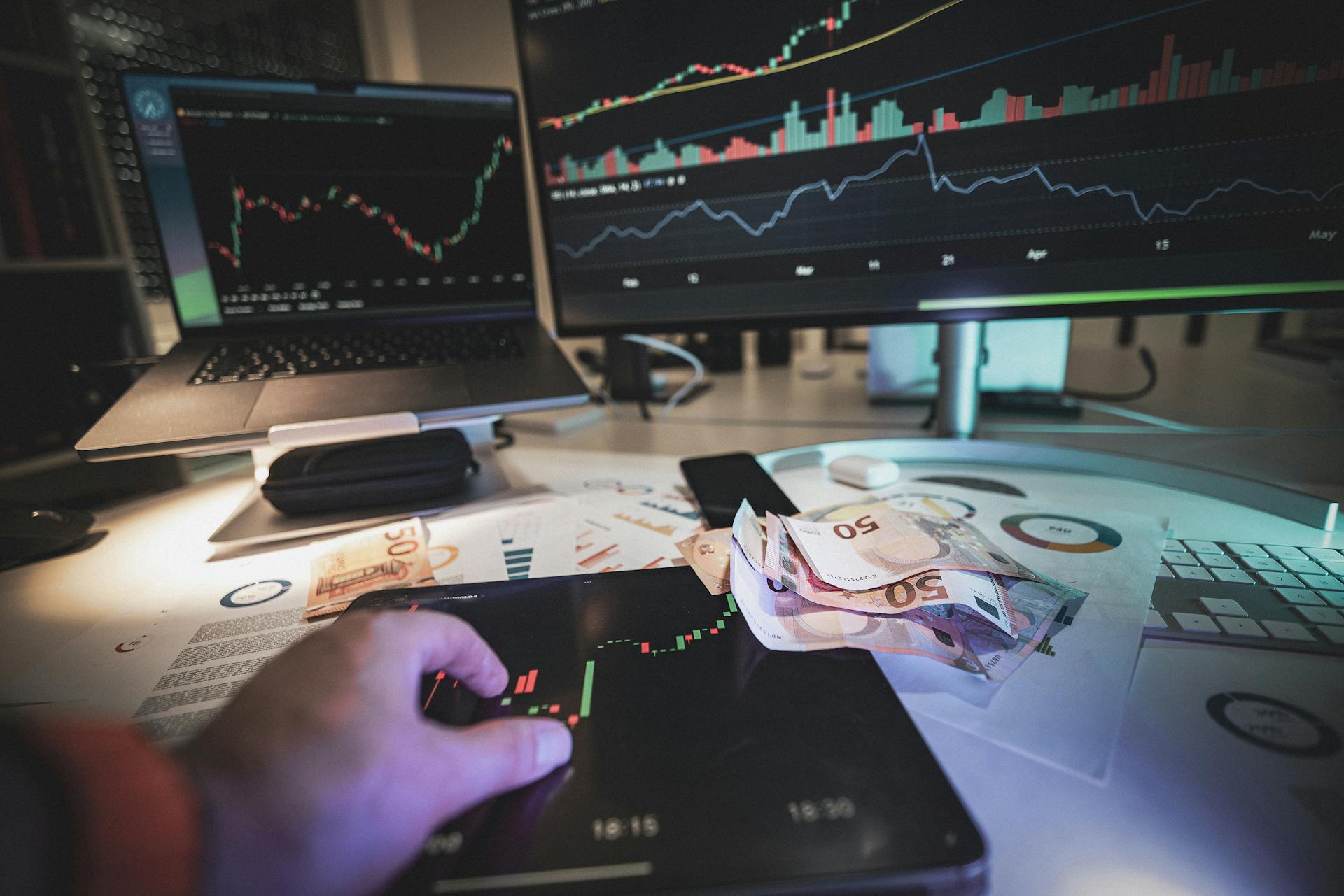 Hand on tablet displaying stock quotes. Euro cash currency.