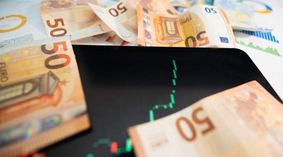 Close-up of euro banknotes beside a digital stock market chart on a tablet, representing the monetary value of pip movements