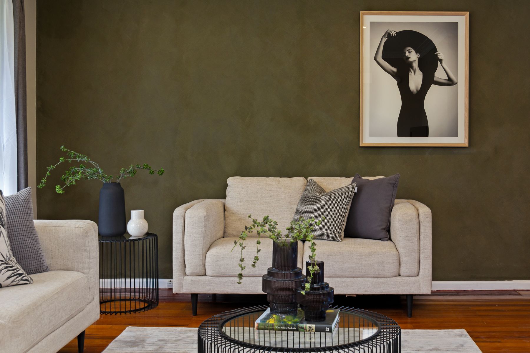 Contemporary apartment living room with muted green walls, beige sofa and black-framed artwork