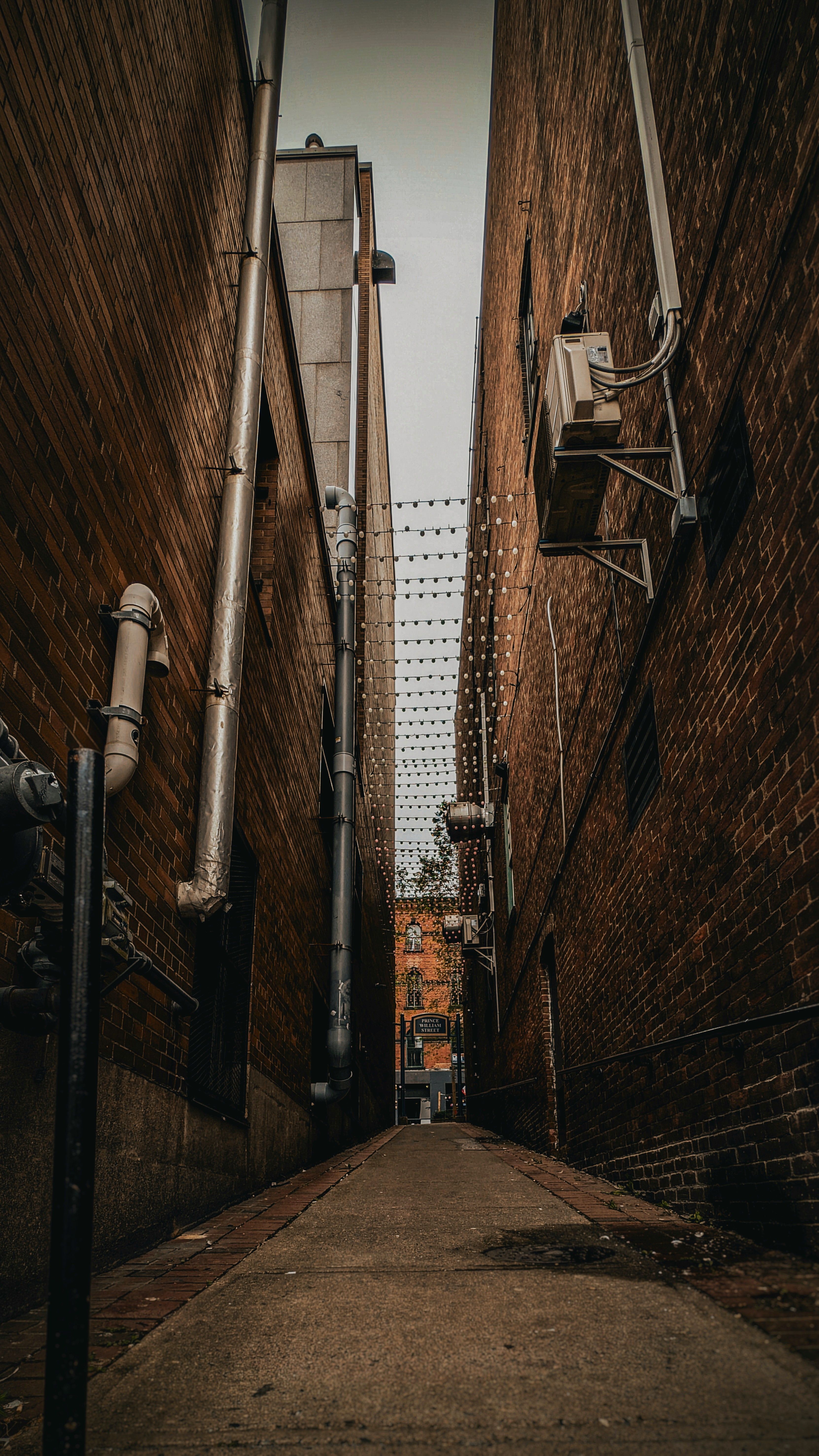 A narrow alley with a brick wall and a fire hydrant · Free Stock Photo