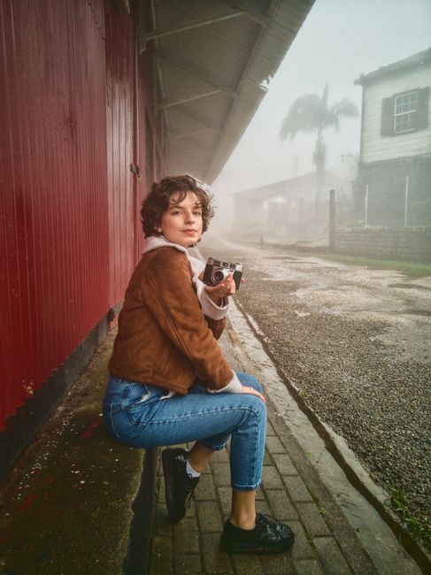 A woman in a foggy urban setting holds a vintage camera, showcasing early fall fashion.