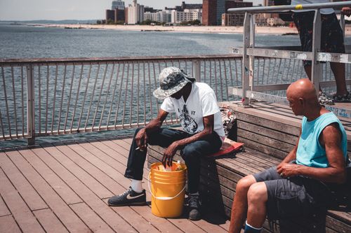 Free Two men enjoy a relaxing day on a riverfront pier with a scenic city view. Stock Photo