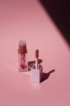 Chic and minimalist image of pink lip gloss and applicator with shadows on a pink surface, perfect for cosmetics themes.