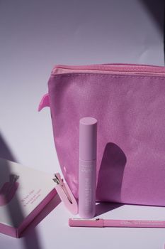 A collection of pink cosmetic products including a makeup bag, lipstick, and packaging in soft lighting.