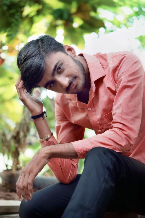 Free Casual portrait of a young man in a coral shirt, sitting outdoors on a sunny day. Stock Photo
