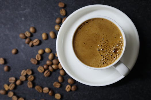 Cup of rich espresso surrounded by scattered coffee beans on a dark backdrop, ideal for morning caffeine themes.