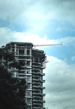 High-rise building under construction with crane against a cloudy sky.