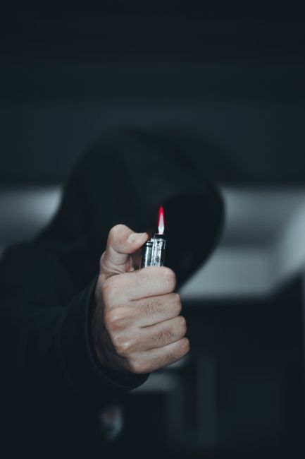 A hooded figure in a dark setting holding a lit lighter, creating a sense of mystery and suspense.