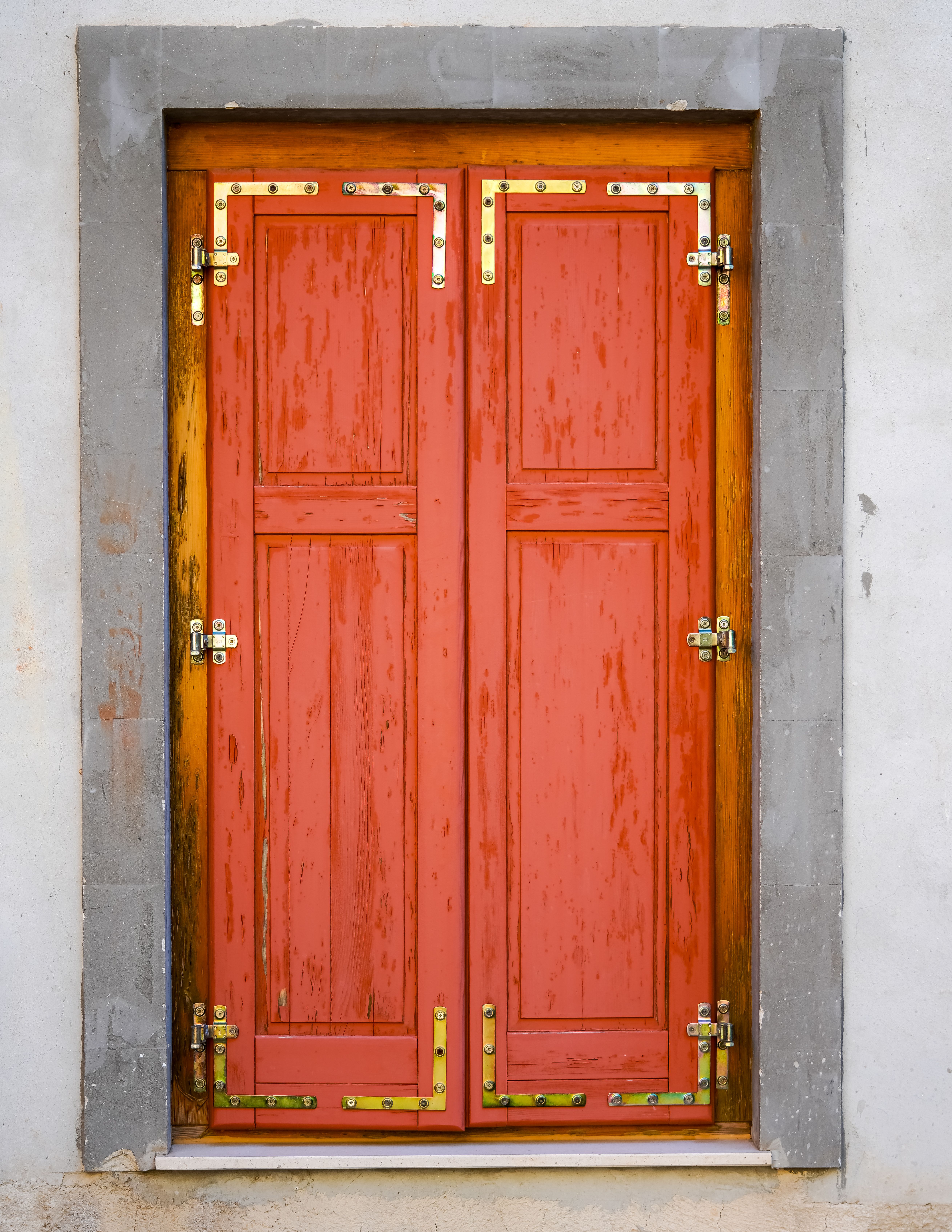 A classic wooden door with vibrant red paint and brass hinges in a stone frame, exuding vintage charm.