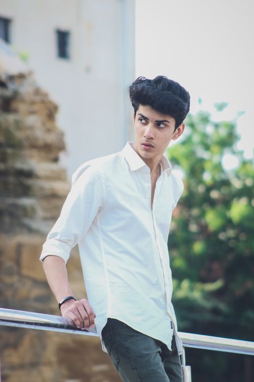 Free A young man in a white shirt and casual attire leans outdoors, looking thoughtful. Stock Photo