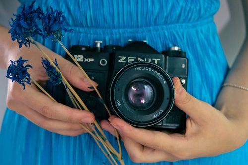 Free A woman in a blue dress holds a vintage Zenit camera with dried flowers, embodying retro charm. Stock Photo