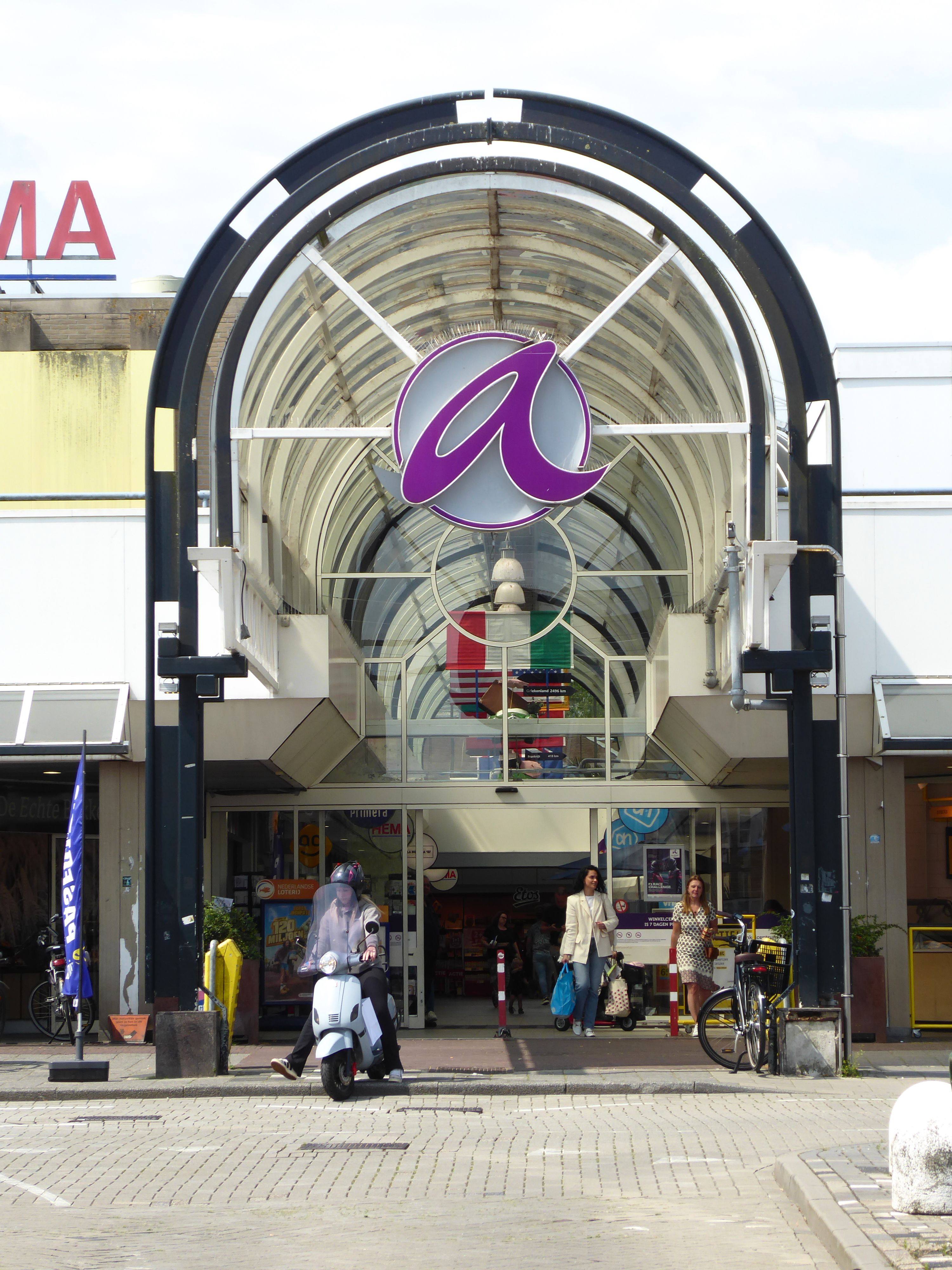 A bustling shopping center with a distinct arched entrance and modern architecture.