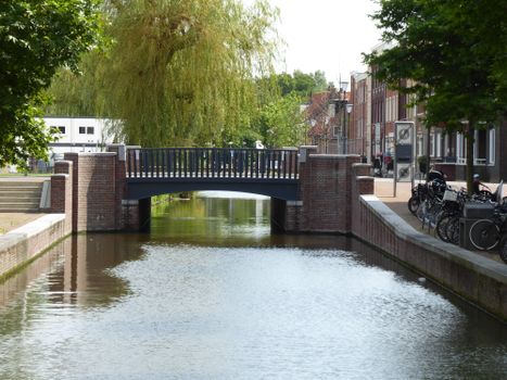 A picturesque urban canal scene with a classic bridge and lush trees in a cityscape setting.