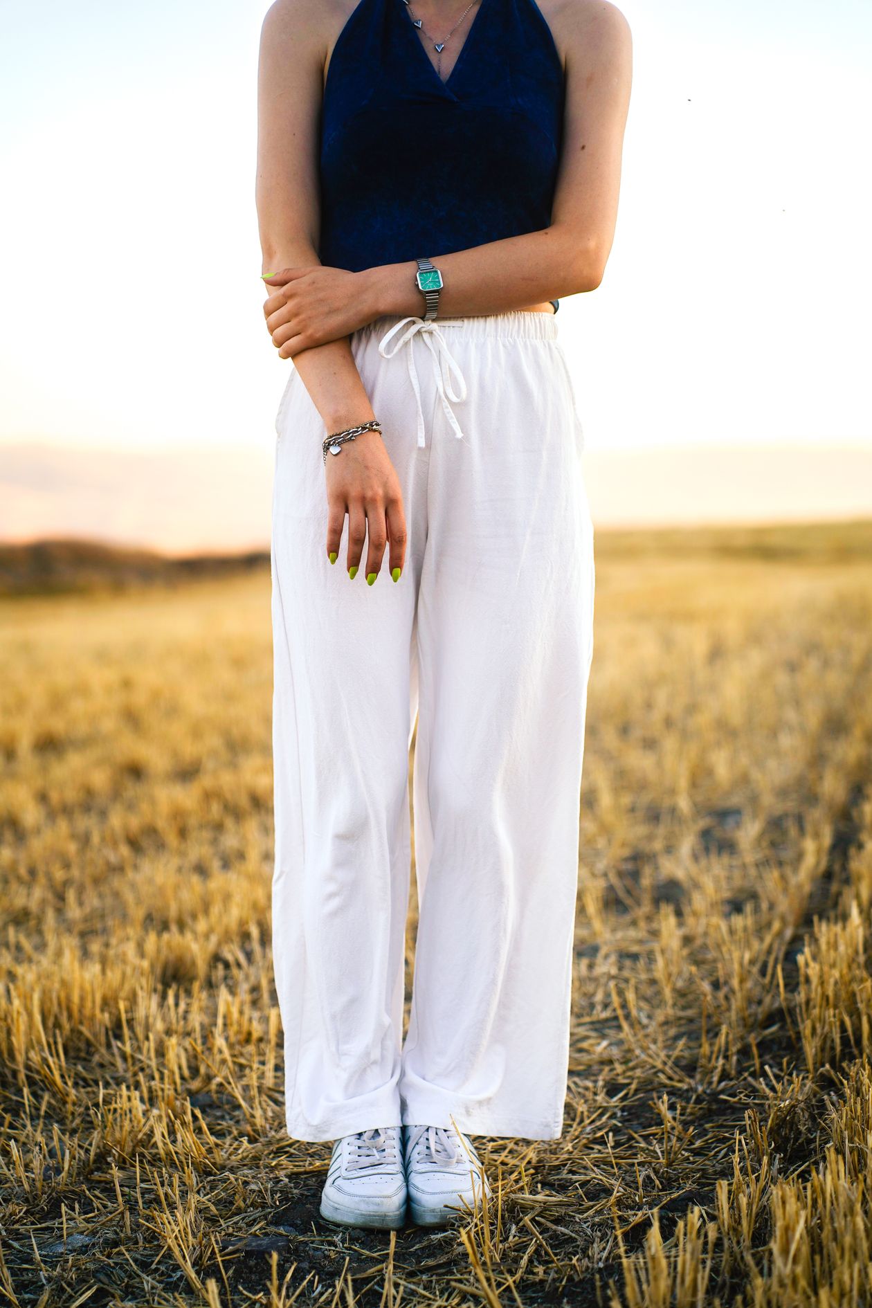 Woman wearing white wide-leg drawstring pants with a navy halter top in a field at sunset