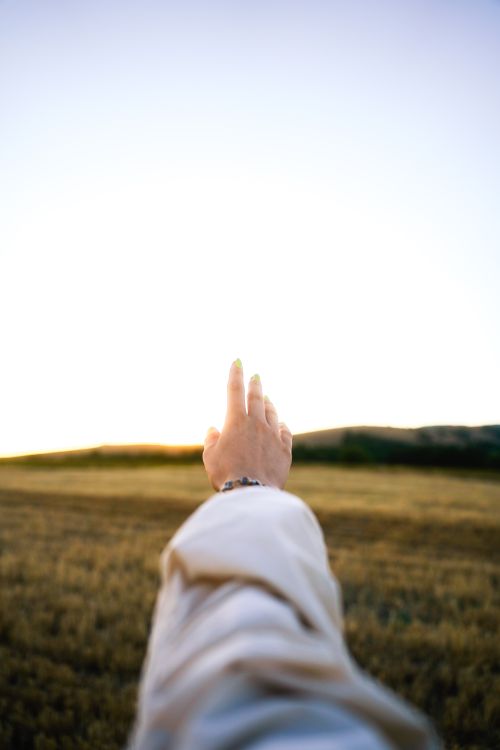 Free A hand reaching out towards the sky in a peaceful rural field setting. Stock Photo