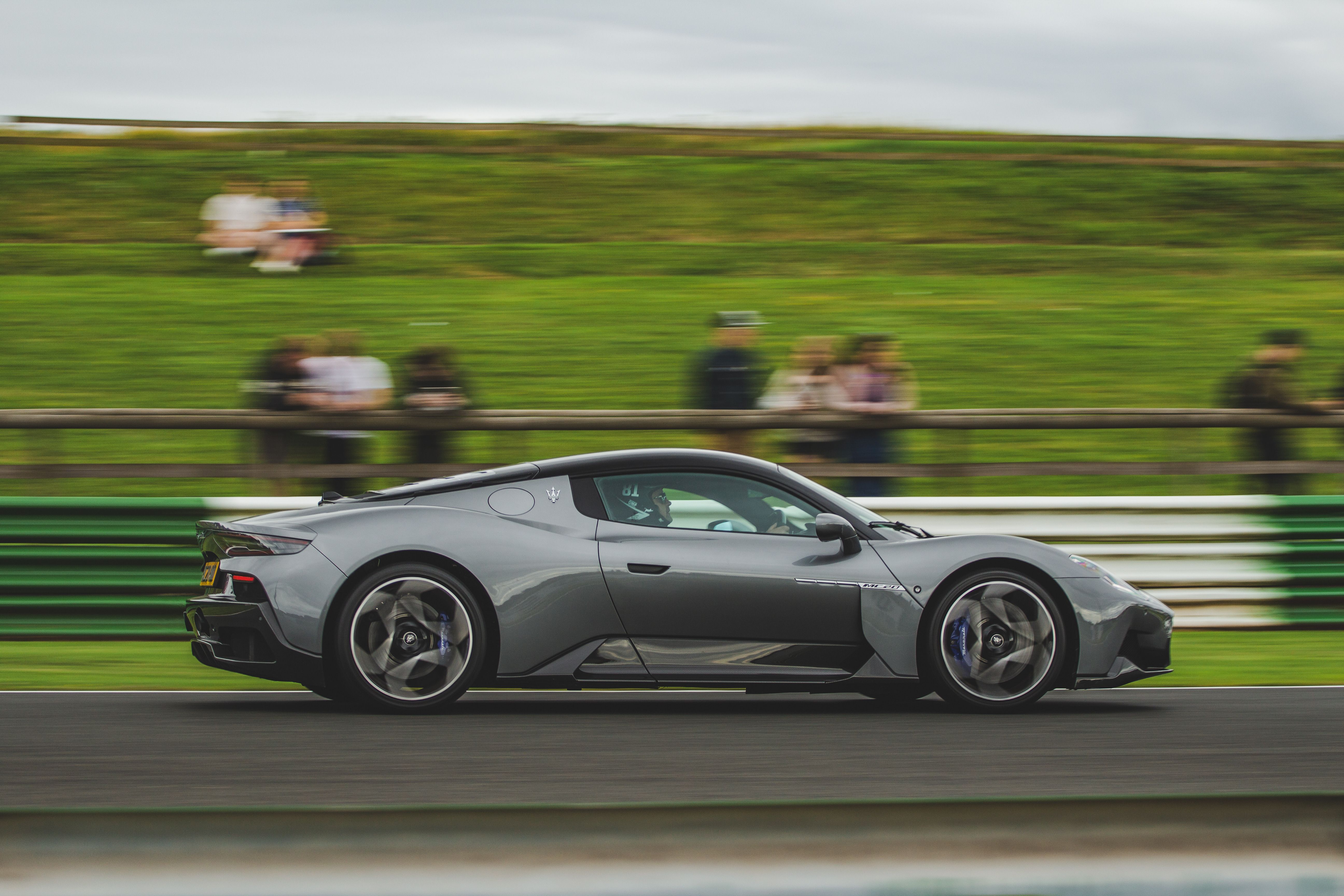 Fast sports car racing on a track with a blurred green field behind it.