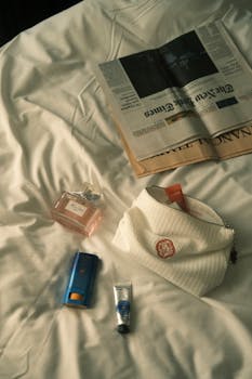 A cozy arrangement featuring perfume, cosmetics, and a newspaper on a bed, creating a luxurious ambiance.