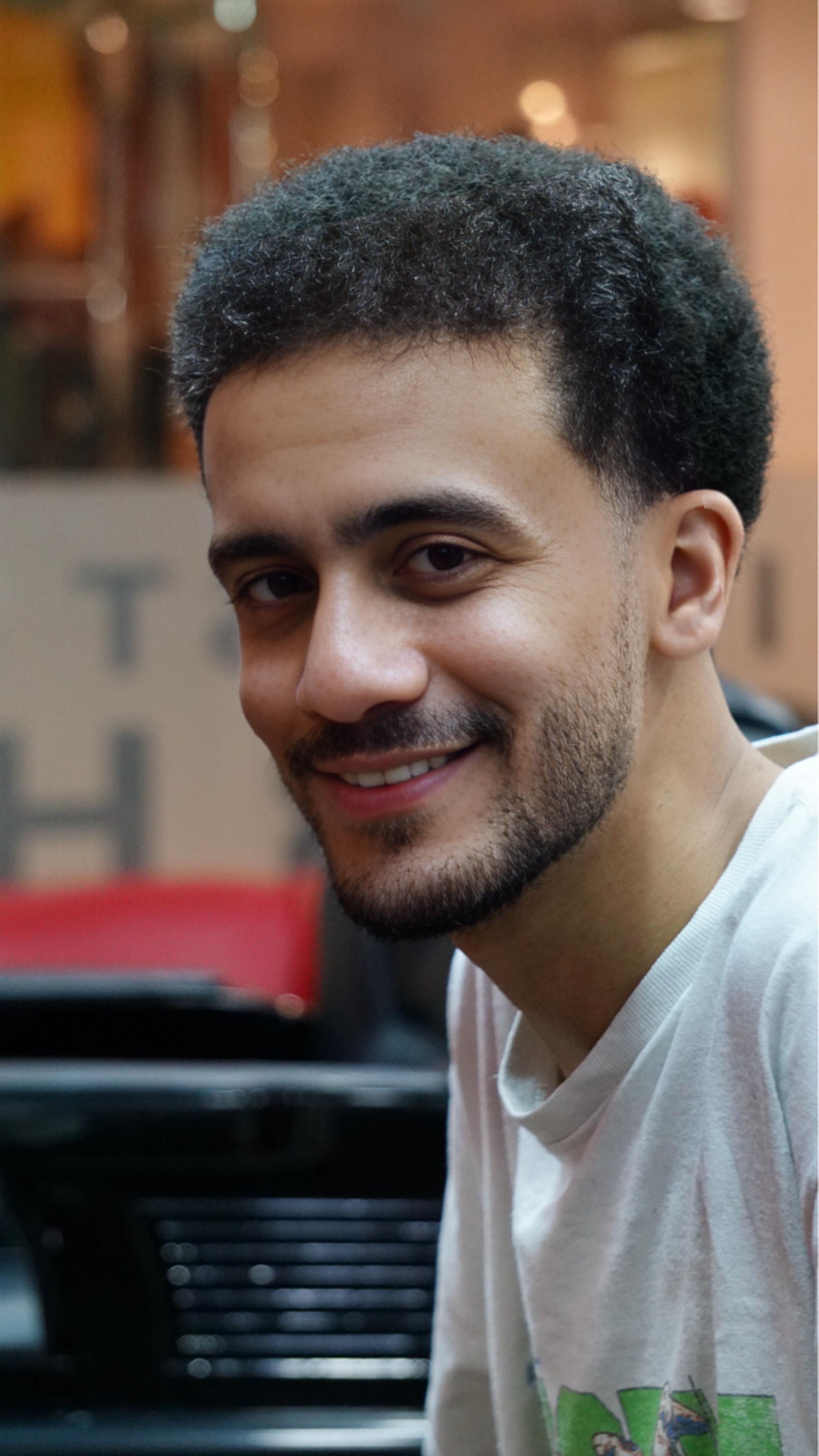 Portrait of a smiling young man with facial hair in an indoor setting, exuding confidence and warmth.