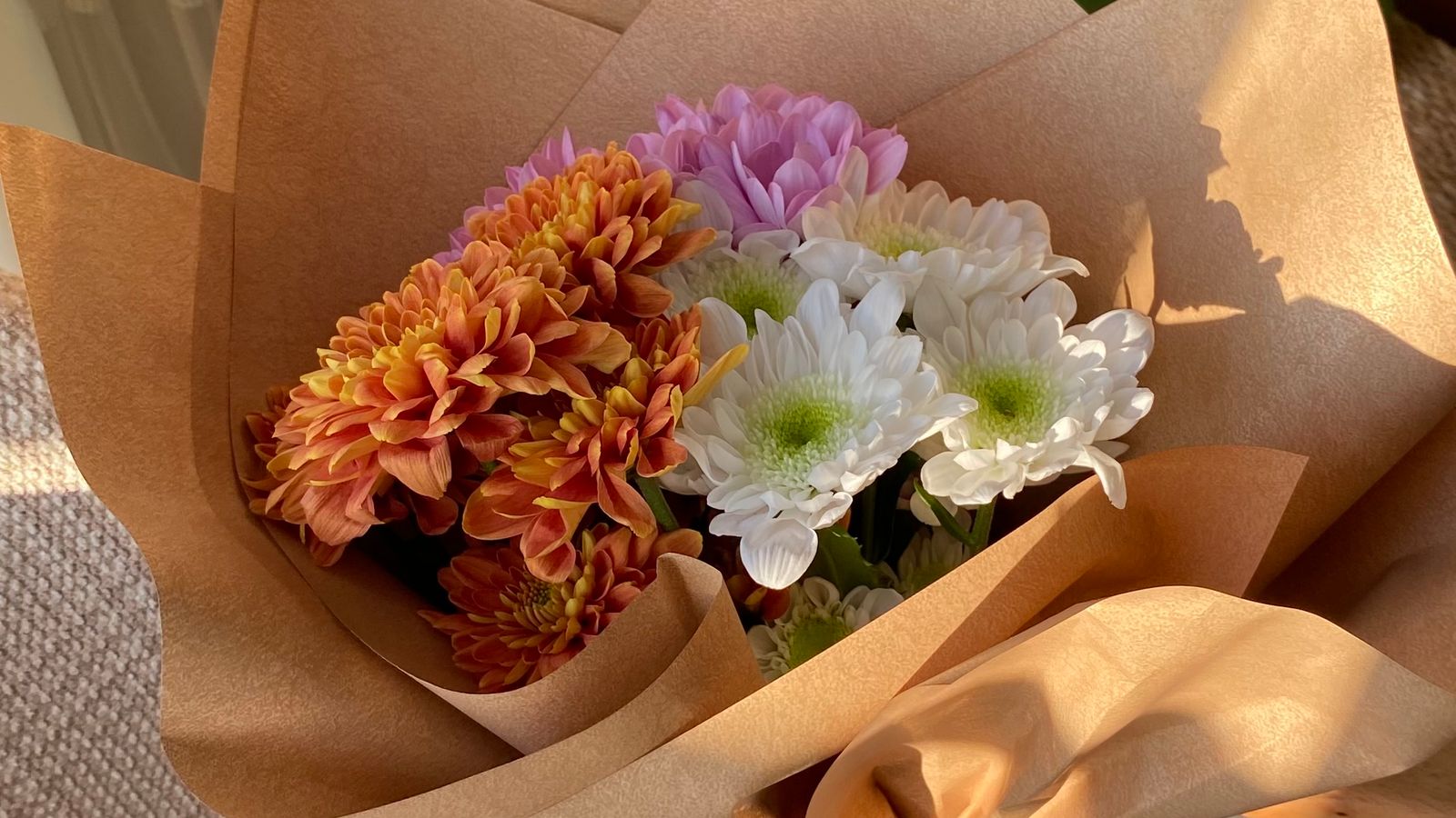 Orange, white and purple flowers wrapped in brown paper on a chair